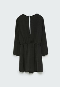 Combinaison noire à manches longues avec une taille froncée et une fente verticale dans le dos, maintenue par une petite fermeture à bouton en haut.