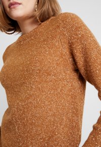 Brauner Strickpullover mit strukturiertem Finish, runder Halslinie und langen Ärmeln, mit dezenten weißen Sprenkeln.