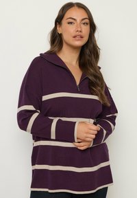 Lila gestreifter Pullover mit Halb-Reißverschluss-Kragen, der beigen horizontalen Streifen aufweist. Weiches Material, lockere Passform und lange Ärmel.