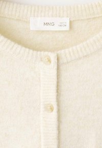 Světlobéžový cardigan z měkkého materiálu s žebrovaným výstřihem, vybavený třemi kulatými knoflíky a štítkem s velikostí 9-10 let.