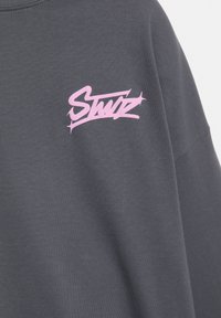 Szürke pamut crew nyakú pulóver, a mellkason rózsaszín, stilizált logóval. Simás tapintású és normál szabású.