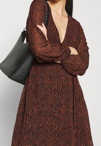 Brun och svart randig klänning med djup V-ringning och svävande ärmar, i kombination med en texturerad svart axelväska.