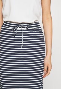 Marinblå och vit randig kjol med elastisk midja och snörning. Har en slät yta och knälång design.