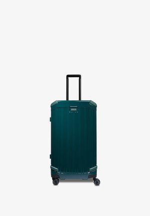 Valigia rigida color teal scuro con texture a coste verticali, manico telescopico nero e quattro ruote nere per la mobilità.