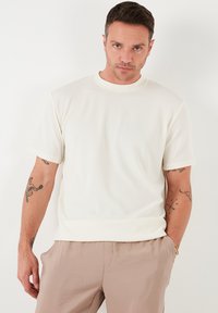 Hvid ribbet kort�ærmet t-shirt med rund halsudskæring, iført med lysebrune bukser. Har en afslappet pasform og struktureret overflade.