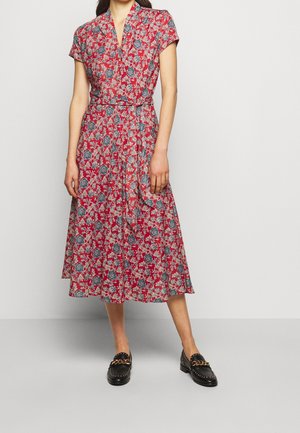 Kvinde iført en rød blomsterprint midi slå-om-kjole kombineret med sorte loafers med guldkæde-detaljer.