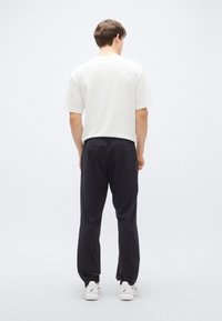 Fehér pamut póló és fekete melegítőnadrág, mindkettő laza szabású. A pólónak rövid ujjú, a melegítőnadrágnak rugalmas derékpántja és puha tapintása van.