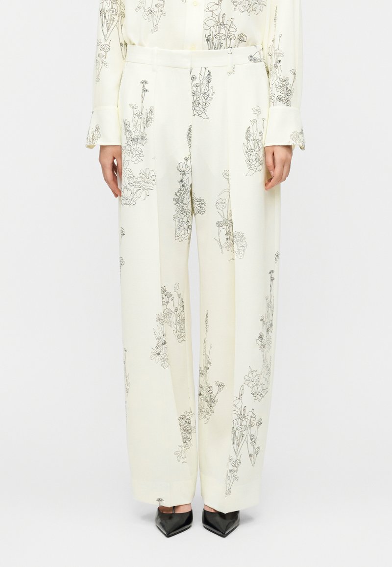 Παντελόνια με φαρδύ πόδι σε κρεμ ύφασμα με μαύρα λουλουδάτα περίγραμμα, άνετη εφαρμογή, λεία υφή και θηλιές ζώνης με καθαρό σχέδιο.