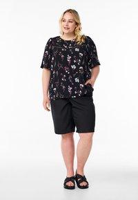 Blusa nera a fiori con maniche corte, caratterizzata da vivaci motivi floreali; abbinata a pantaloni corti neri e sandali neri con cinturini.