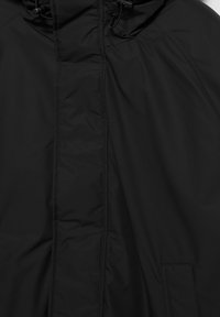 Jachetă neagră cu umplutură, cu fermoar și închidere cu nasturi, având glugă cu șnururi ajustabile.