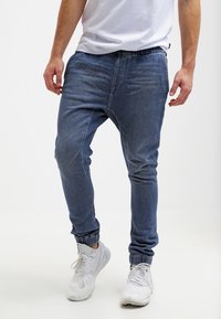 Džínové joggery v modré barvě, s elastickým pasem, manžetami na kotnících a volnějším střihem. Hladká textura s jemnými prvky vyblednutí.