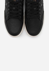 Baskets en cuir noir avec une finition texturée, semelle blanche contrastante et design classique à lacets. Comprend un bout renforcé et des œillets en métal.