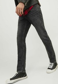 Jeans de denim negros con un corte ajustado, que presentan un ligero desgaste, costuras en contraste y bolsillos frontales. Combinados con zapatillas de caña alta negras.