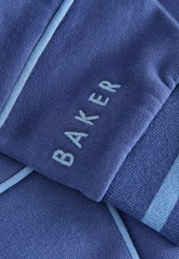 Sinine kudumine, millel on helesinised detailid ja tikandiga "BAKER" tekst. Omab pehmet tekstuuri ning kihilist disaini kontrasteerivate triipudega.