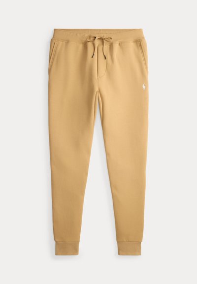 Tan sweatpants made of soft fabric with an elastic waistband, drawstring, two side pockets, and ribbed cuffs. Small logo on the front.