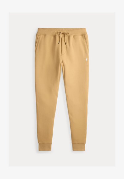 Tan sweatpants made of soft fabric with an elastic waistband, drawstring, two side pockets, and ribbed cuffs. Small logo on the front.