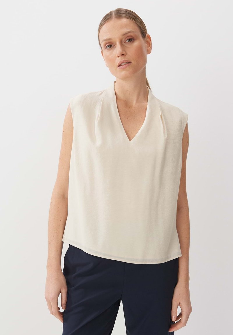 Blusa senza maniche color crema con scollo a V e sottili pieghe sulle spalle, caratterizzata da una texture liscia e una vestibilità rilassata e ampia.