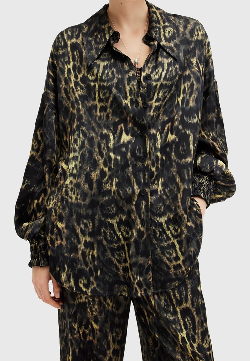 Personne portant une chemise ample à manches longues boutonnée et un pantalon assorti avec un motif léopard noir et or.