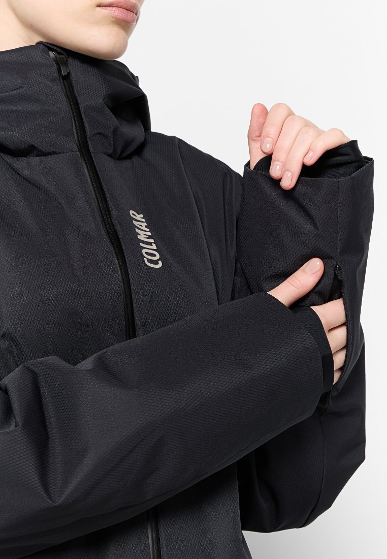 Giacca impermeabile nera con tessuto testurizzato, colletto alto e polsini con zip. Presenta il logo prominente "Colmar" sul davanti.