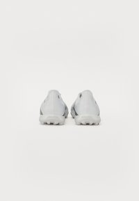 Graue und weiße Fußballschuhe mit einer strukturierten Oberfläche, kontrastierenden Akzenten und einem markanten Sohlendesign für Traktion, von hinten betrachtet.