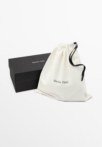 Petite pochette en coton de couleur crème avec le logo "Massimo Dutti" imprimé, accompagnée d'une boîte rectangulaire noire portant la même marque.
