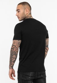 Sort crew neck t-shirt lavet af bomuld, tætsiddende design, korte ærmer, glat tekstur, båret med slidte denimjeans og bemærkelsesværdige tatoveringer på armene.