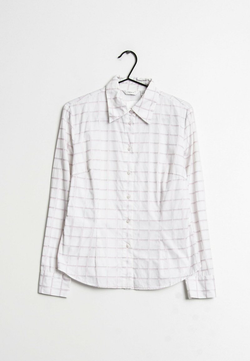 Chemise blanche à boutons avec manches longues et motif à fines carreaux roses, suspendue sur un cintre noir sur un fond blanc.