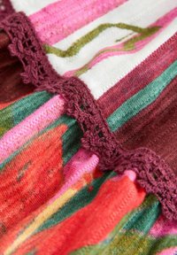 Gros plan sur un tissu rayé multicolore avec des sections rouges, vertes, roses et blanches, avec une bordure en crochet bordeaux.