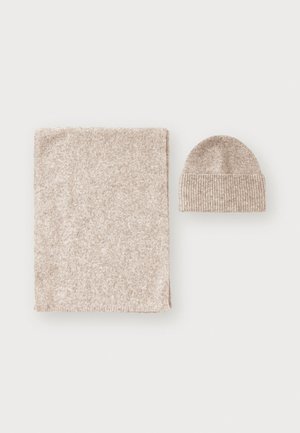 Beige knit blanket and matching beanie, both soft and textured, with the blanket being rectangular and the beanie featuring a ribbed design.