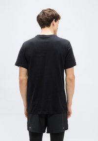 Μαύρο βαμβακερό t-shirt με κοντά μανίκια, στρογγυλή λαιμόκοψη και άνετη εφαρμογή, εμφανίζεται από την πίσω πλευρά. Λεία υφή, μινιμαλιστικός σχεδιασμός.