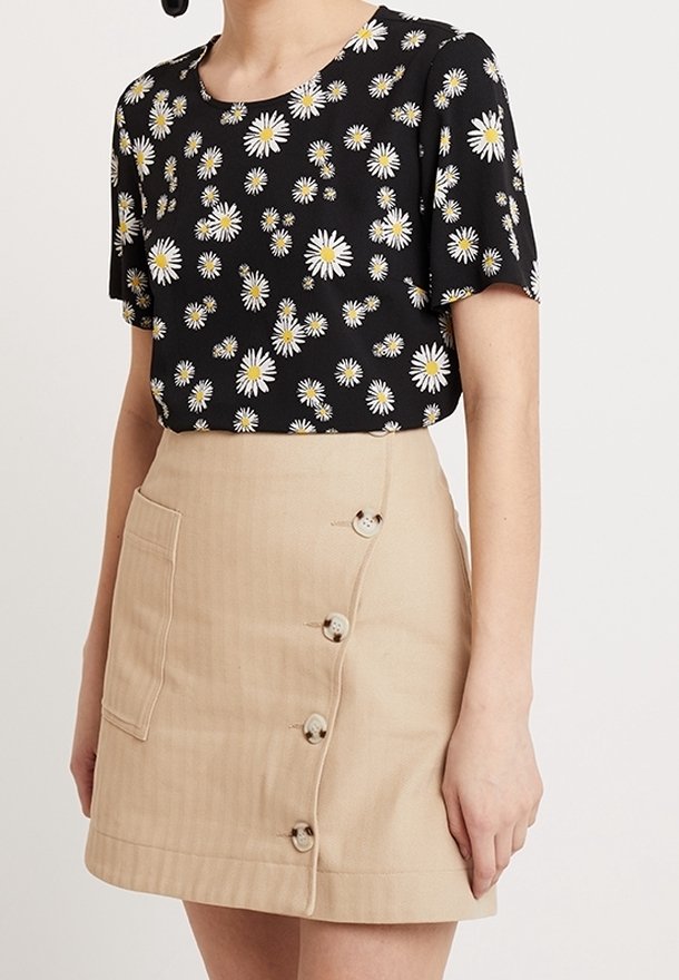 Svart kortärmad topp med vit och gul prästkrageprint; beige inslagsskjol med sidoficka och fem dekorativa knappar.