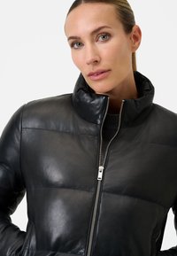 Sort læderjakke med høj krave, quiltet design og sølvfarvet lynlås. Glat tekstur med minimalistisk stil og ingen synlige mønstre.