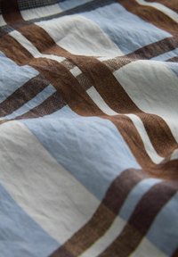 Tkanina o pomarszczonej fakturze z geometrycznym wzorem niebieskich, białych i brązowych nakładających się prostokątów i pasków.