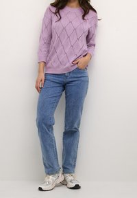 Ljuslila stickad tröja med diamantmönster, tillsammans med ljusblå raka jeans och grå sneakers med vita detaljer.