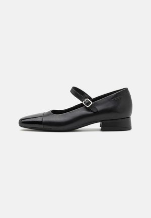 Zapatos Mary Jane de cuero negro con puntera de charol, correa de tobillo ajustable y tacón bajo. Textura suave y diseño elegante.