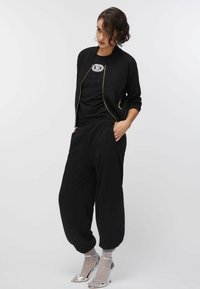 Mustast bomberjaki kuldse tõmblukuga, kombineeritud musta T-särgiga, millel on hõbedane logo, laiad mustad püksid, hõbedased kontsakingad ja hallid sokid.