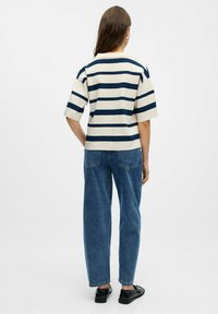 Randig topp i kräm och marinblå, med en boxig passform och korta ärmar, i kombination med lösa blå jeans och svarta skor. Slät textur genom hela plagget.
