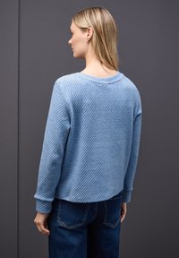 Hellblauer Pullover mit Struktur, Rundhalsausschnitt, langen Ärmeln und leicht kurzem Schnitt, kombiniert mit dunkelblauen Jeans.