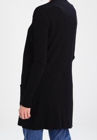 Langer schwarzer Rippstrickcardigan mit hohem Kragen, langen Ärmeln und seitlichen Taschen, aus strukturiertem Strickstoff gefertigt.