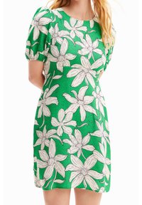 Groene jurk met een bloemenpatroon van witte bloemen en zwarte omtrekken. Korte puffmouwen en een ronde halslijn. Soepele textuur.