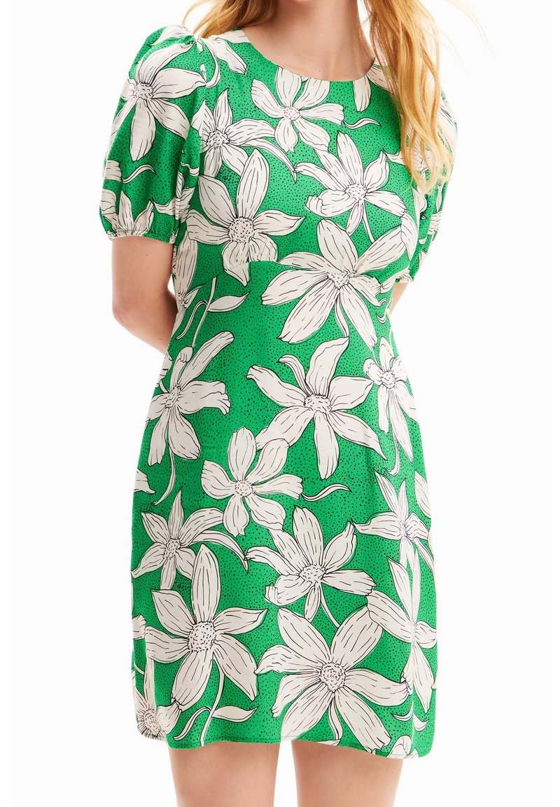 Groene jurk met een bloemenpatroon van witte bloemen en zwarte omtrekken. Korte puffmouwen en een ronde halslijn. Soepele textuur.