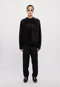 Μαύρη φουντωτή μπλούζα με τύπωμα "COUTURE", συνδυασμένη με μαύρα παντελόνια και χοντρά μαύρα αθλητικά παπούτσια. Τα αξεσουάρ περιλαμβάνουν λευκά γυαλιά ηλίου.