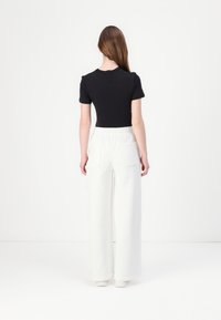 Top negro ajustado de manga corta combinado con pantalones anchos blancos que cuentan con una cinturilla elástica y dos bolsillos traseros.