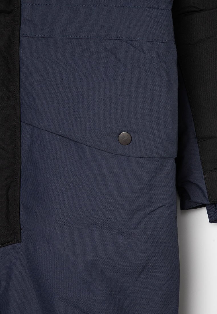 Mörk marinblå vadderad jacka med svarta detaljer, försedd med tryckknappar och en slät, texturerad yta.