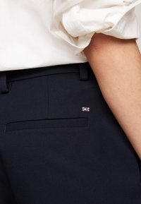 Pantaloni blu navy con una texture liscia, dotati di una tasca posteriore e di un piccolo logo multicolore accentuato vicino alla vita. Design classico e su misura.
