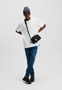 Biely tričko s krátkym rukávom, modré džínsy, čierne topánky a šedá pletená čiapka. Taška cez telo s čiernou tkaninou a modrými akcentmi.