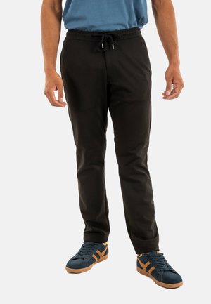 Zwarte stretchbroek met een loungelint in de taille, slim fit, voorzakken en gecombineerd met donkerblauwe sneakers met oranje accenten.