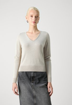 Pull en V beige clair en tissu doux avec des manches longues, ourlet côtelé, associé à une jupe en jean gris foncé. Design simple et minimaliste.