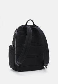 Sac à dos noir avec une texture rembourrée et des accents lisses. Il dispose de bretelles réglables, d'une poignée supérieure et d'une poche latérale zippée.