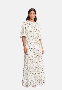Maxikjole i hvitt stoff med blomsterprint i beige og brune nyanser. Løs passform og vide ermer, som gir en flytende silhuett.